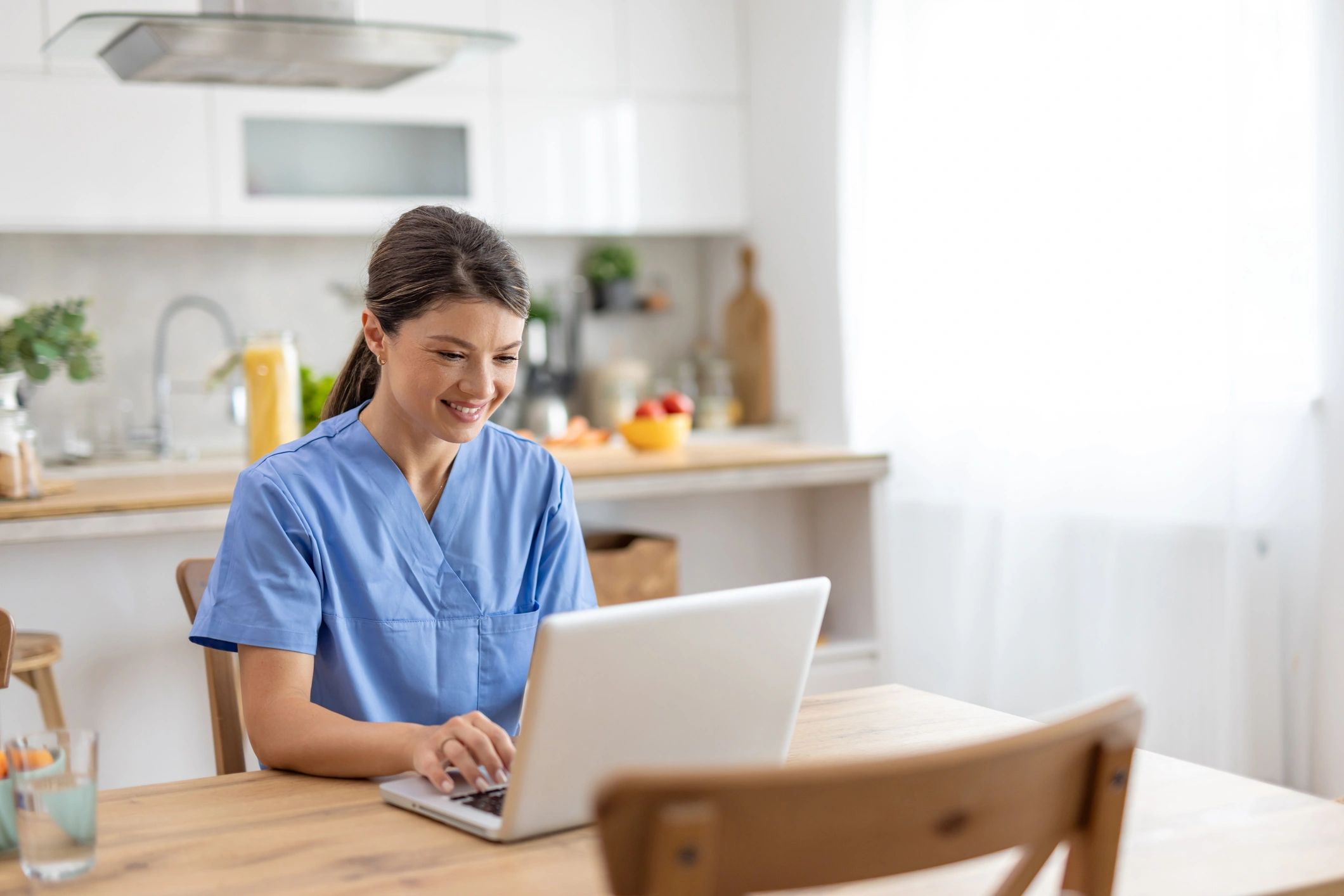 Person in medical scrubs using a laptop at home